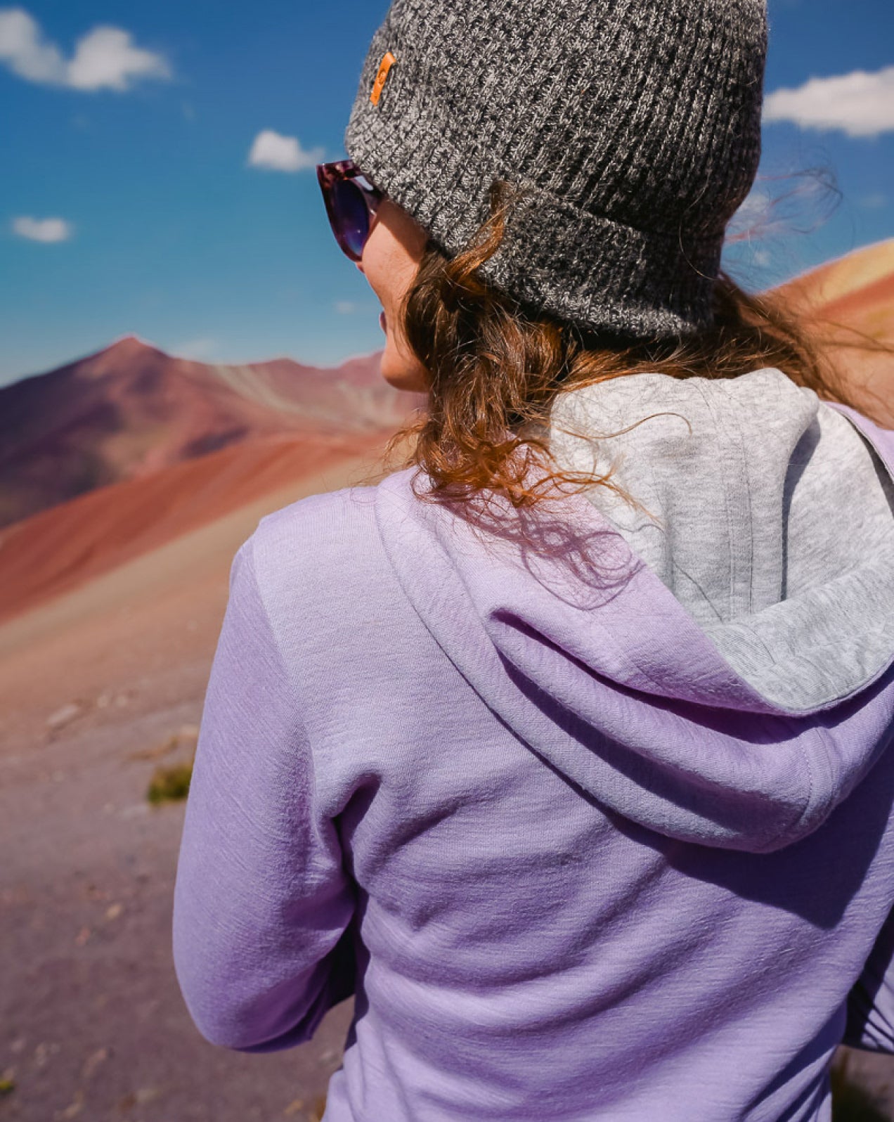 A woman wearing our lavender Breathe Women's Hoodie in front of the Rainbow Mountain in Peru