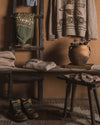 Woven sweaters and boots on a wooden shelf against a brown wall.