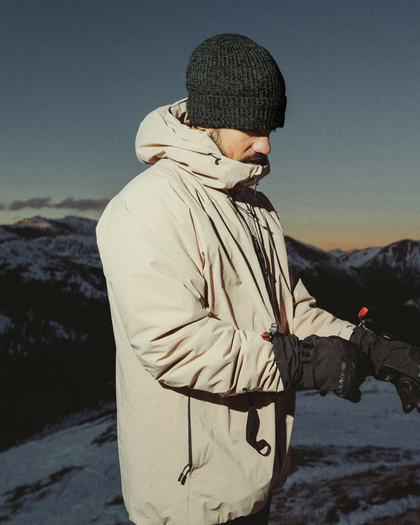 Person in a beige coat and the Andean Moss Cozy Marled beanie standing in a snowy landscape with mountains in the background.