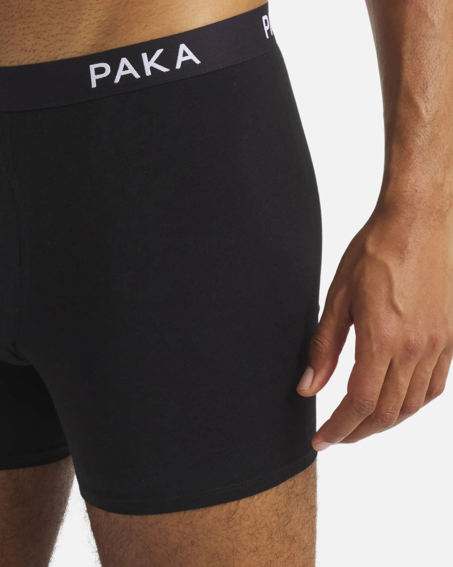 Close-up side view of Men’s Essential boxer brief in black on model showcasing PAKA branded waistband and mid-thigh length on white background