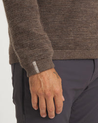 Close-up of a person wearing a brown sweater and dark pants on a white background