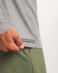 Close-up of Men’s Sol Crew long sleeve alpaca shirt showing side seam and woven hem detail with model’s hand and green pants