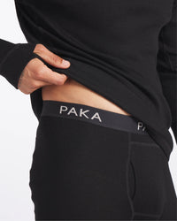 Close Up of Man Lifting Shirt to Show PAKA Text on Black Alpaca Wool Thermal Baselayer Pants – PAKA Apparel
