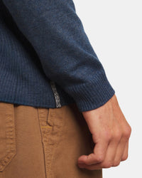 Close-up of Men’s Ultralight Crew showcasing ribbed sleeve cuff and woven side-seam tag with model’s hand and brown pants in background