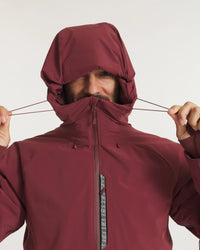 Close-up front view of Men’s Apu Parka showcasing adjustable hood being tightened and high zip collar with patterned chest pocket on a light studio background
