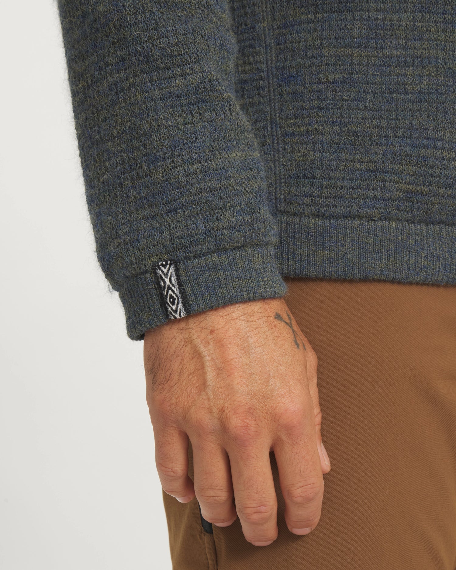 Close-up of a person wearing a textured green sweater with a brand logo on the sleeve against a white background.