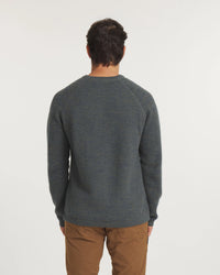 Person wearing a green sweater and brown pants on a white background