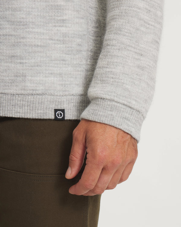 Close-up of a person wearing a  Light Grey sweater with brand logo