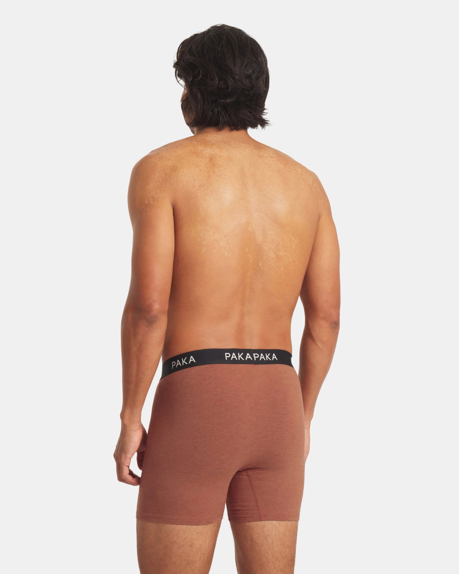 Man wearing brown boxer briefs with a visible brand logo on a white background