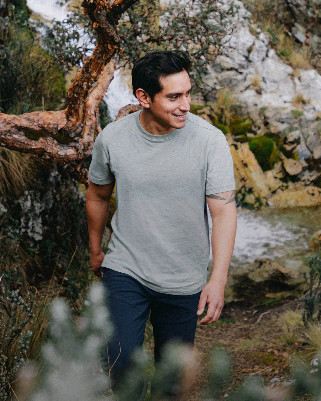 Man walking outdoors in a natural setting with trees and rocks.