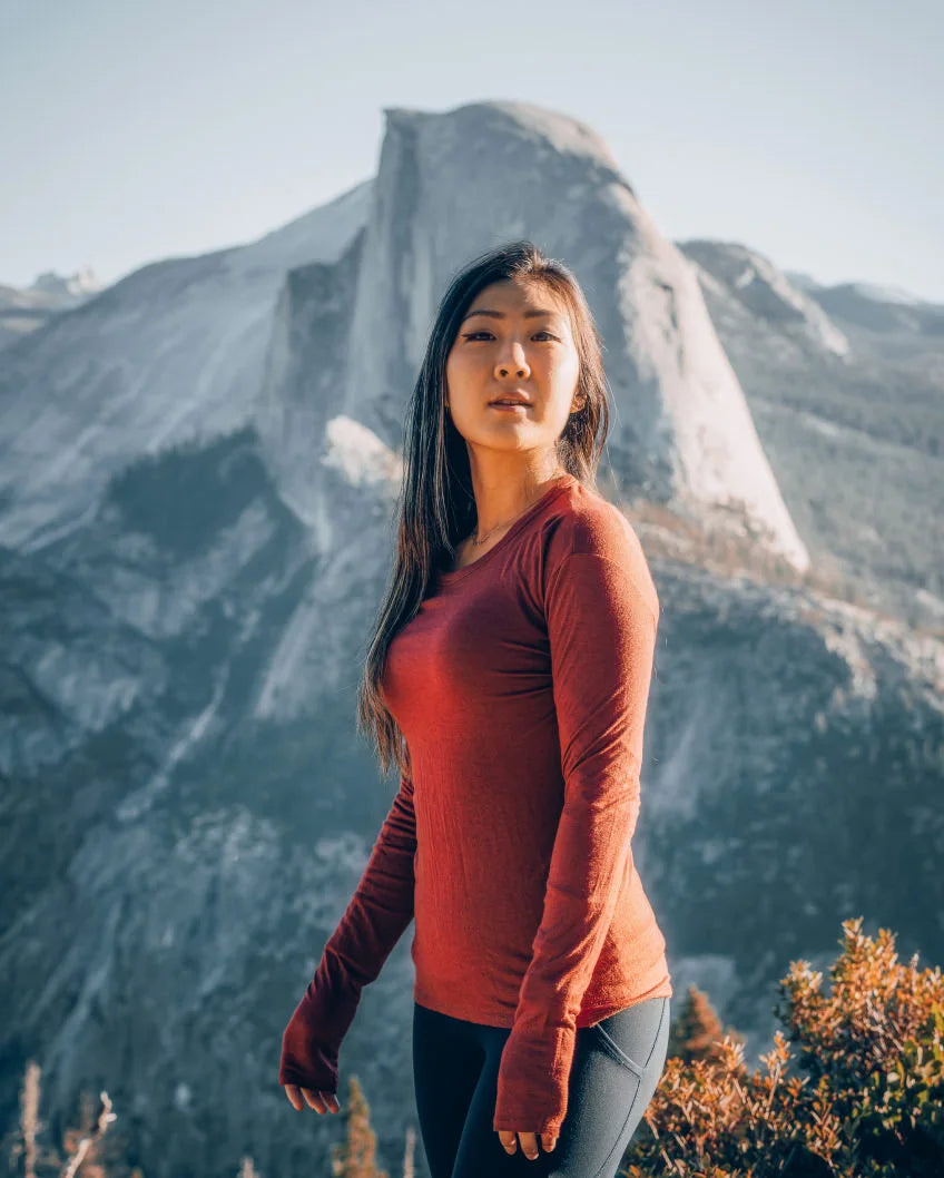 A Woman wearing a clay baselayer with a mountain behind her