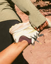 Person pulling on purple ankle alpaca socks while trail running on a red dirt path