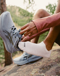 Close up side view of white Trail Ankle Socks on model showing ankle height, snug fit, and PAKA logo with trail background