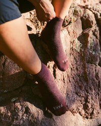 Close-up of Trail 1/4 crew socks in charcoal on model’s feet on a rocky trail showing mid-ankle height and textured knit