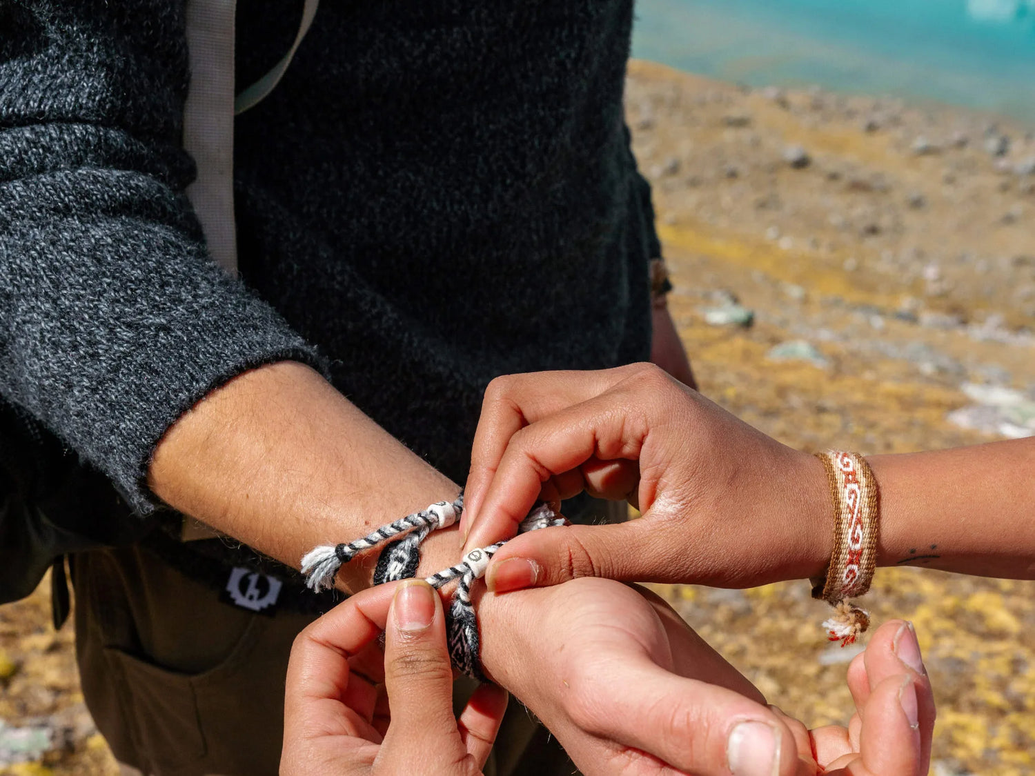 Tying an alpaca bracelet by a lake