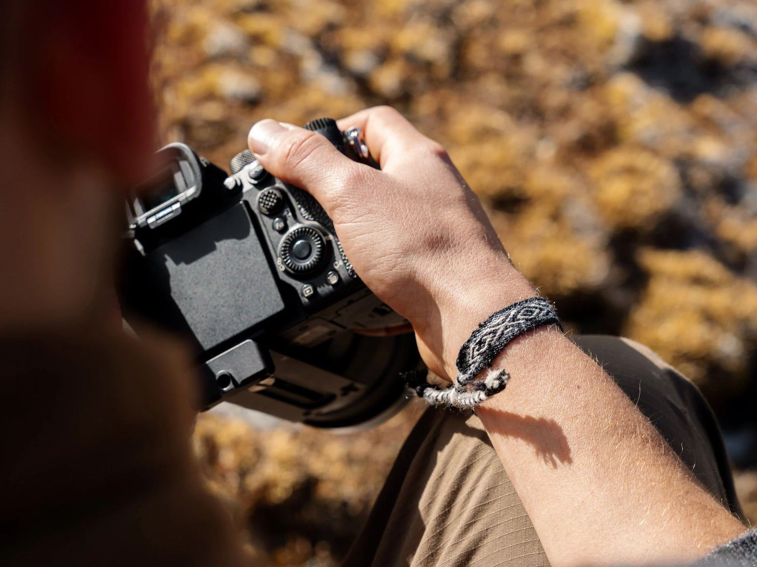 A man holding a camera. In his right hand, he wears an alpaca bracelet