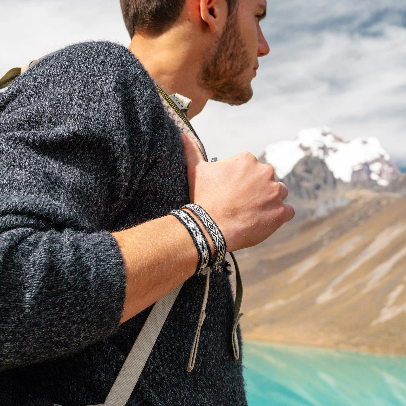 A man wearing two alpaca bracelets in his right hand. He's looking at a mineral blue lake and the mountains