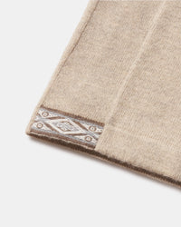 Close-up of The Quarter Zip hem showing beige alpaca knit and decorative patterned trim on a white background