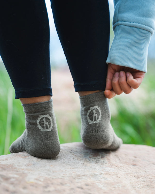 Person Grabbing Top of Forage Grey Trail Alpaca Quarter Crew Breathable Hiking Socks on Right Foot with Stone – PAKA Apparel