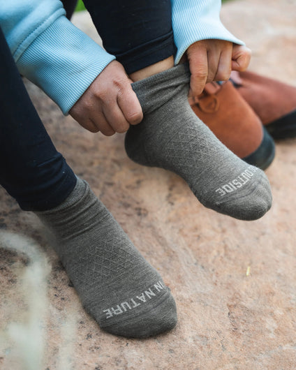 Person Grabbing Top of Forage Green Trail Natural Fiber Alpaca Quarter Crew Socks on Right Foot with Stone – PAKA Apparel