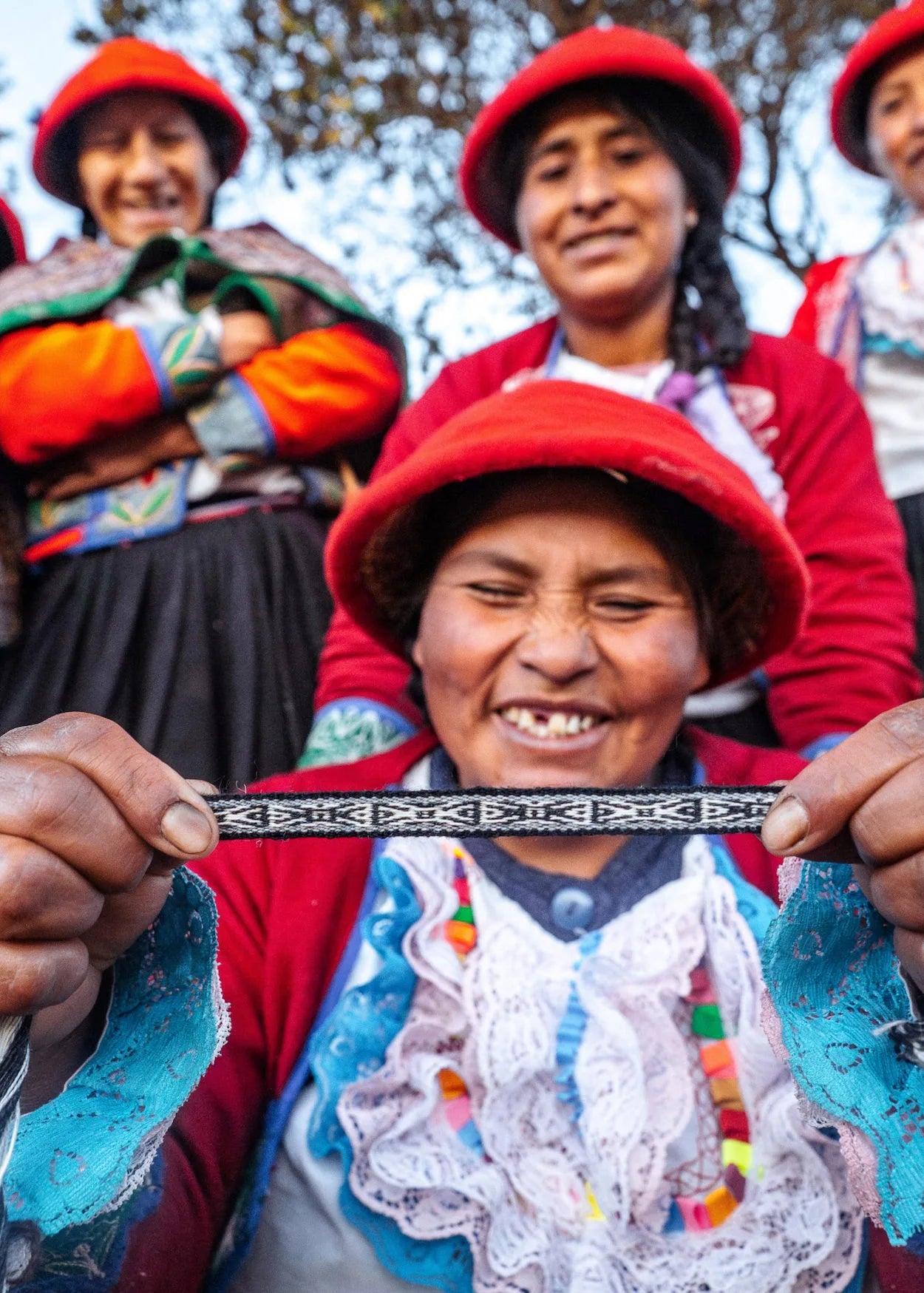 A group of quechua weavers smiling and showing an alpaca bracelet
