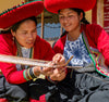 Two Quechua women in traditional costumes weaving colorful alpaca fiber