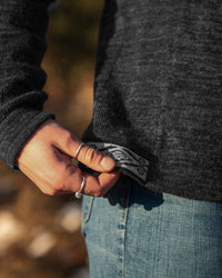 Close-up of The Original Crew alpaca crewneck showing charcoal knit and patterned inner hem with model’s hand and jeans