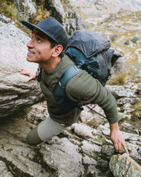 Three-quarter view of The Original Crew alpaca crewneck in eucalyptus on a man, showing soft knit texture and relaxed fit on rocky trail