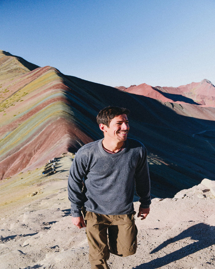 Person standing in front of a colorful mountain range with a clear blue sky.