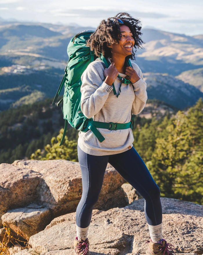 Woman with a green backpack standing on a mountain top with scenic view