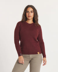 Woman wearing a maroon sweater and beige pants on a white background