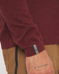 Close-up of a maroon sweater sleeve with a brand logo on a white background