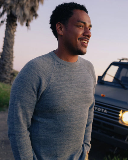 Three-quarter view of The Original Crew alpaca crewneck in bluestone on model showing raglan sleeves and slim fit, outdoor