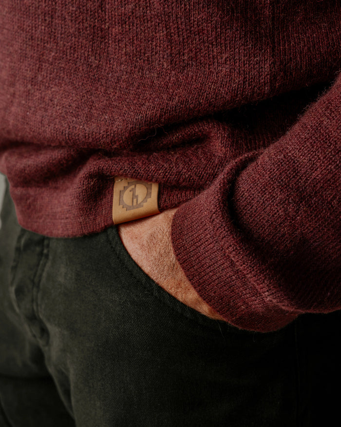 Close-up of a PAKA's The Original Crew in Burgundy with a brand logo on the sleeve, worn over dark pants.