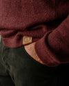 Close-up of a PAKA's The Original Crew in Burgundy with a brand logo on the sleeve, worn over dark pants.