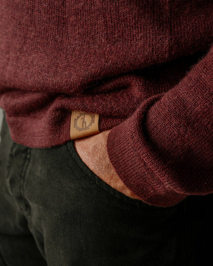 Close-up of a PAKA's The Original Crew in Burgundy with a brand logo on the sleeve, worn over dark pants.
