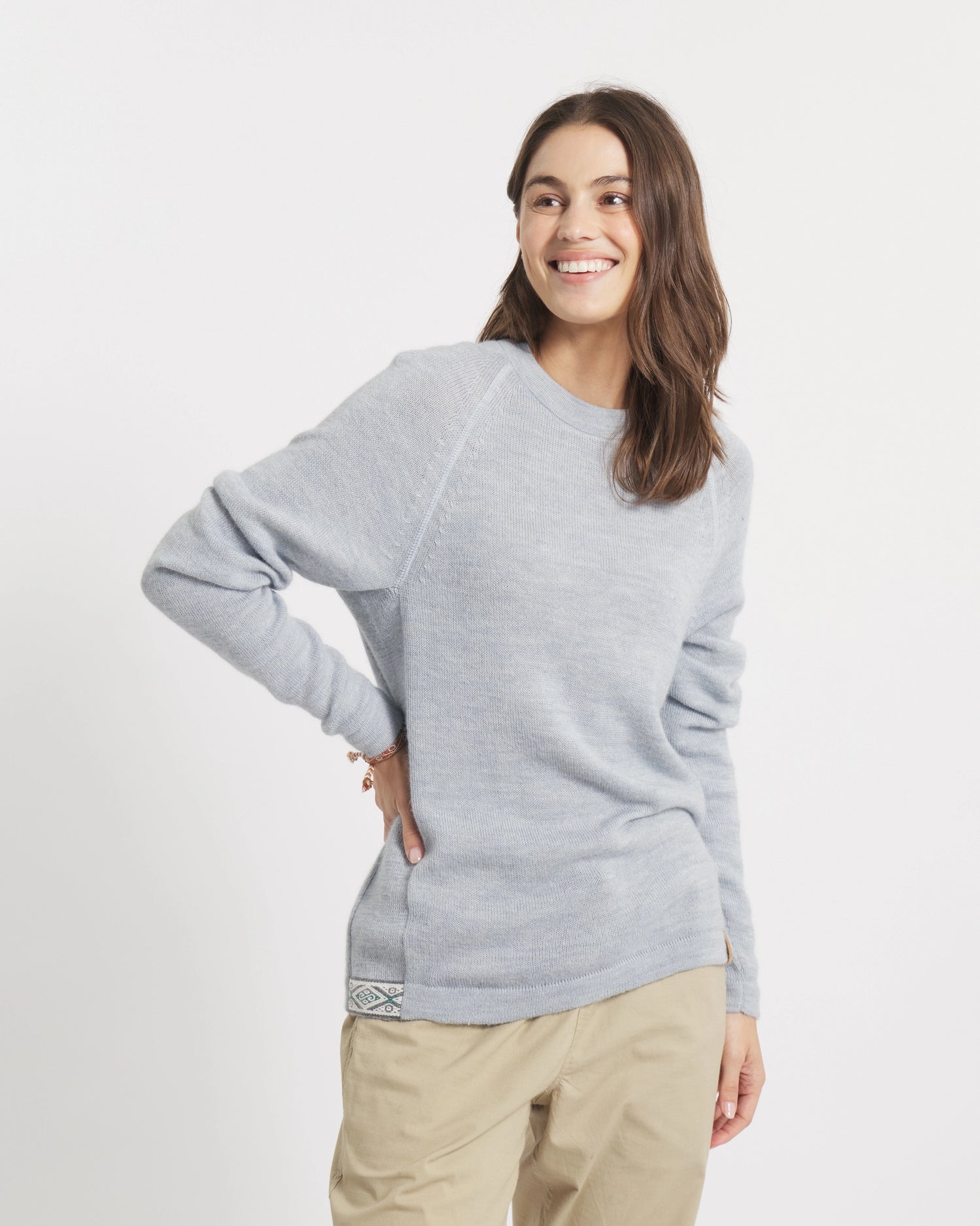Woman wearing a sky blue sweater and beige pants on a white background