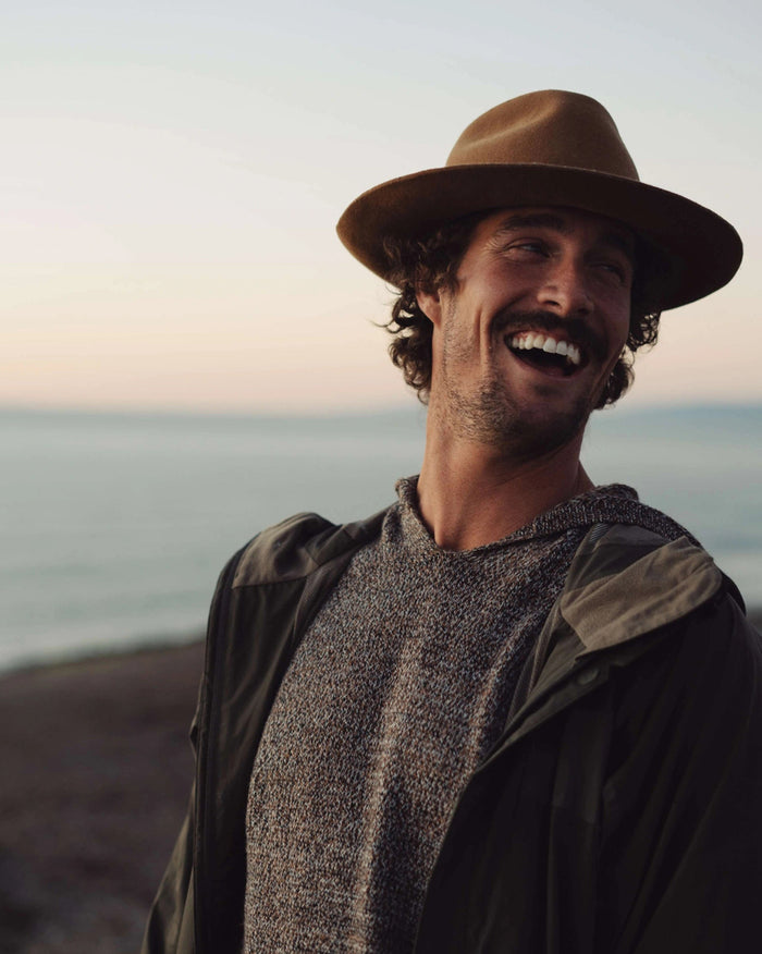 Man wearing a brown hat and jacket standing on a beach with ocean in the background
