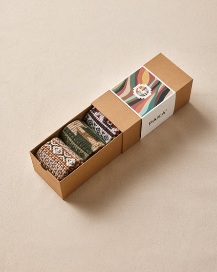 Three patterned socks in a cardboard box with a visible brand logo on a beige background