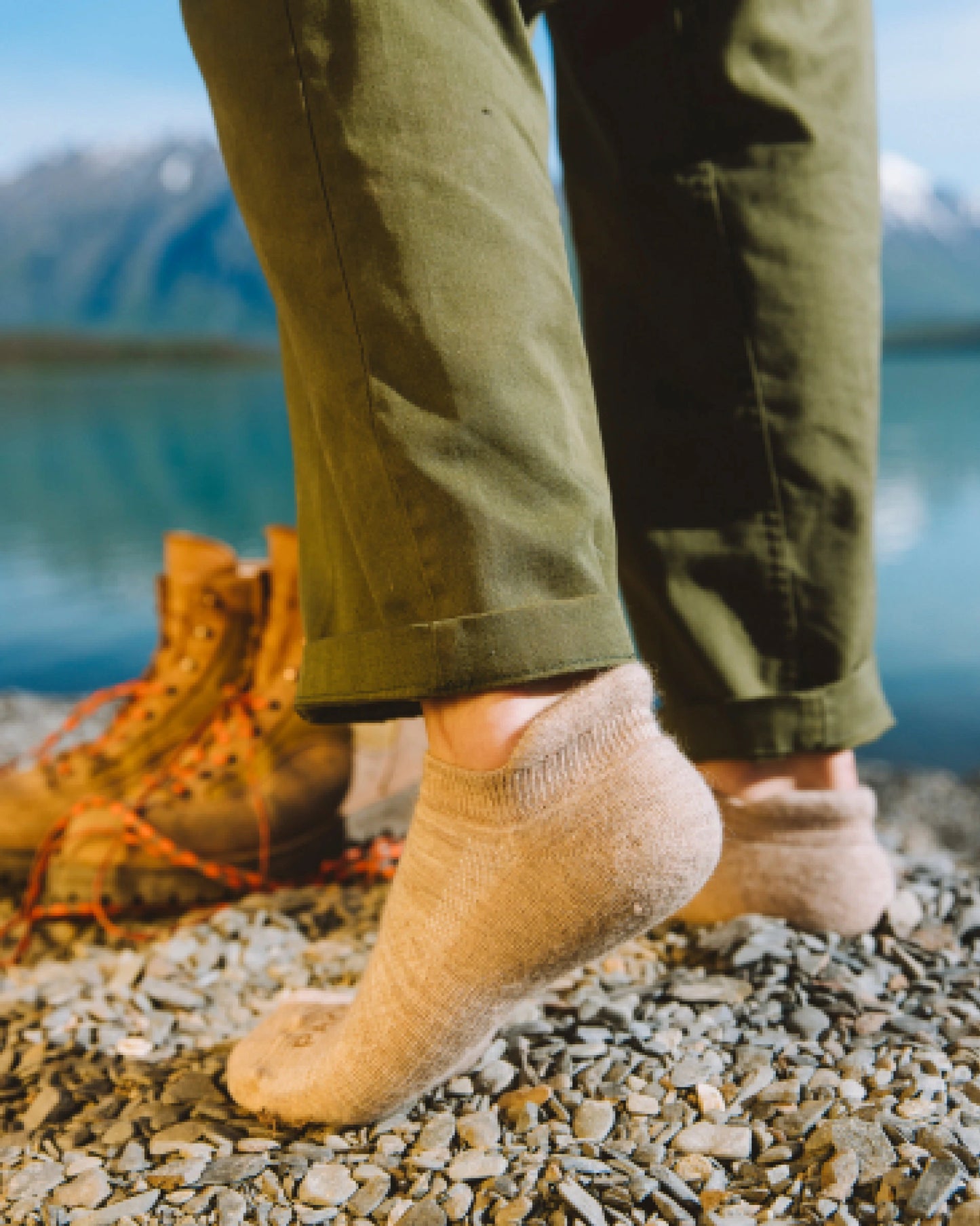 Person wearing tan alpaca ankle socks walking in front of blue lake 