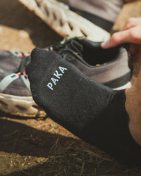 Closeup of Black Trail Alpaca Athletic Ankle Socks on Left Foot with Trail Running Sneakers in Background – PAKA Apparel