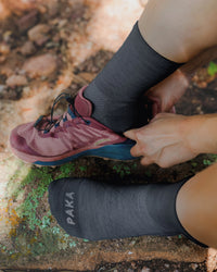Close up of Trail quarter crew socks in charcoal blue on model showing PAKA logo on toe and breathable knit with hiking shoe