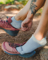 Side view of Trail Ankle Socks (alpaca socks) showcasing low-cut ankle fit and PAKA logo on a dirt trail background