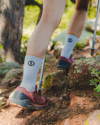 Person hiking on a trail wearing lSilver socks with a logo and dark hiking shoes.