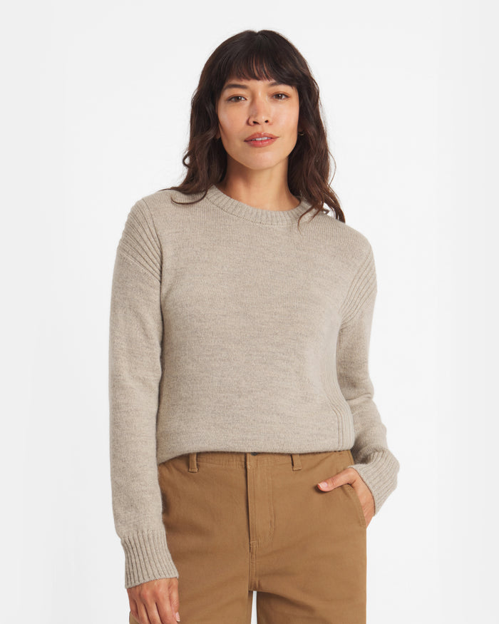Woman wearing a beige sweater and brown pants on a white background