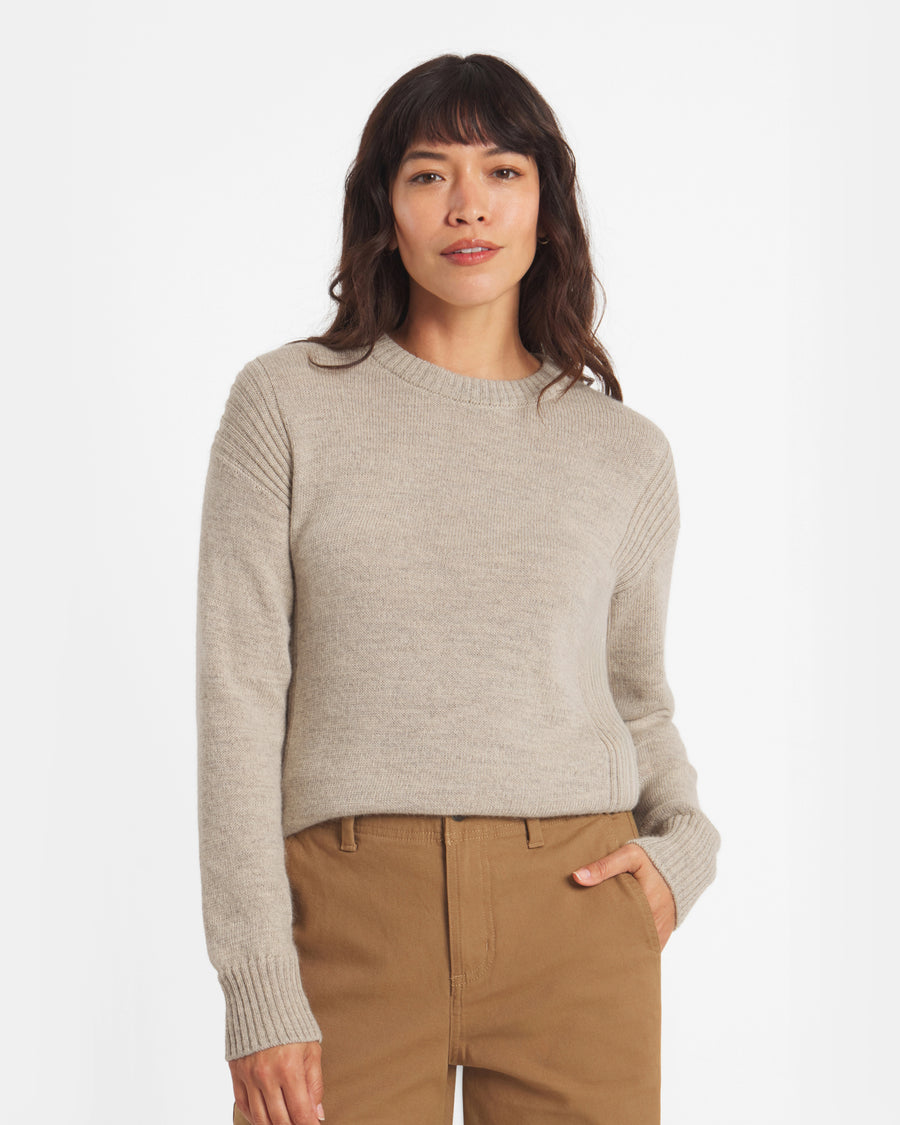 Woman wearing a beige sweater and brown pants on a white background