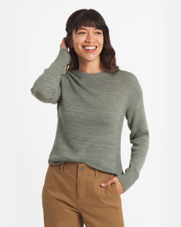 Woman wearing a green sweater and brown pants on a white background