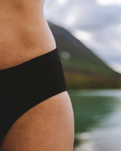 Close-up of Women’s Essential Mid-Rise Brief in black showing mid-rise cut and smooth alpaca fabric on model with lake behind