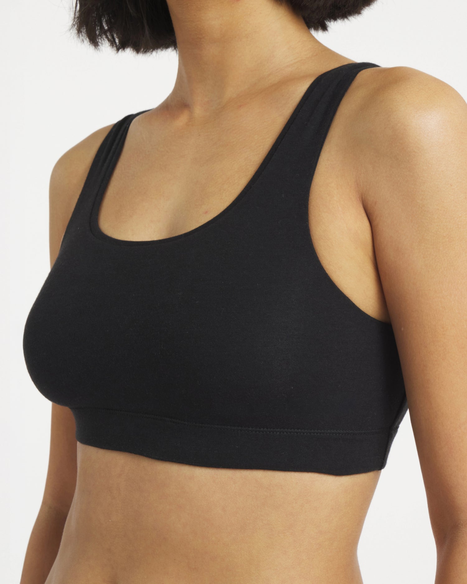 Three-quarter view of black scoop bralette on model, fitted, with scoop neckline, wide straps and elastic underband on white