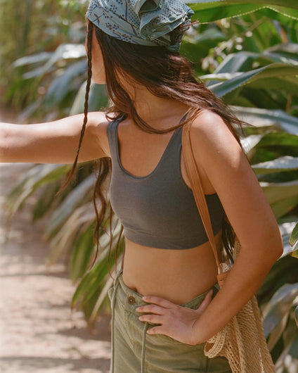 Side view of Women’s Essential Scoop Bralette in Forage on model, fitted, showing scoop neckline, wide straps, and breathable alpaca fabric against a sunlit leafy background